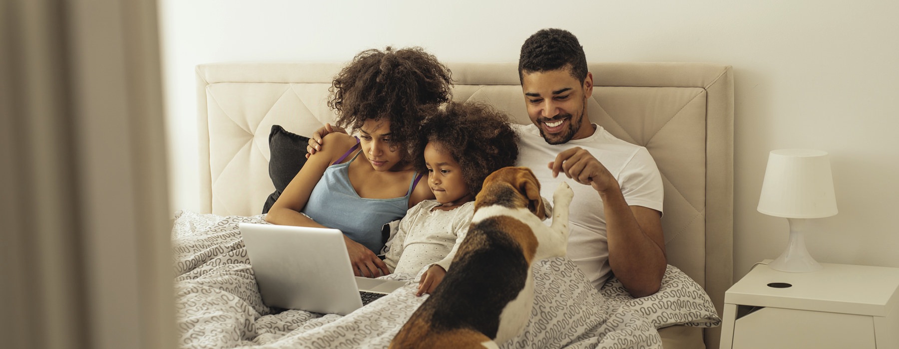 Man, woman, child and dog laying in bed on laptop